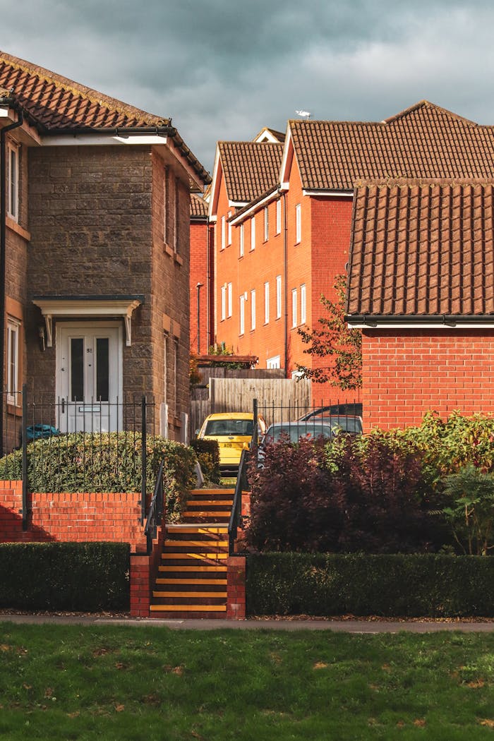 A picturesque suburban scene featuring red brick houses, lawns, and metal stairs under a cloudy sky.